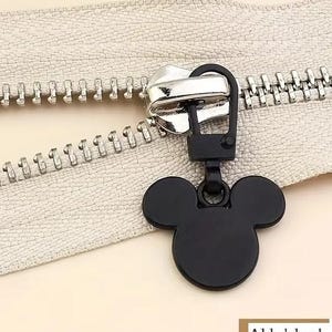Op de afbeelding: Zwarte rits-trekker met een Mickey Mouse-kop ontwerp. De trekker is bevestigd aan een zilveren rits.