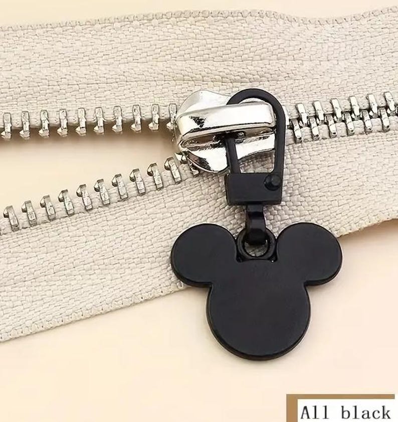 Op de afbeelding: Zwarte rits-trekker met een Mickey Mouse-kop ontwerp. De trekker is bevestigd aan een zilveren rits.