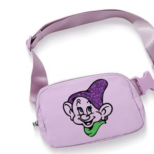 May include: A lilac-coloured fanny pack with a matching adjustable strap and buckle. The front of the bag features a cartoon graphic of a character with a purple glitter hat and green scarf. The bag is designed to be worn around the waist or across the body.