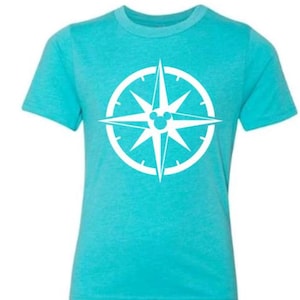 May include: A turquoise t-shirt with a white compass design, incorporating a Mickey Mouse head at the centre. The compass rose is set within a white circle. The shirt has short sleeves and a crew neck.
