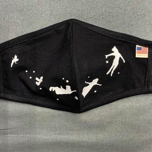 May include: Black face mask with white silhouette figures and stars. The mask has a design of people flying in the sky. A small tag with the American flag is attached to the mask.