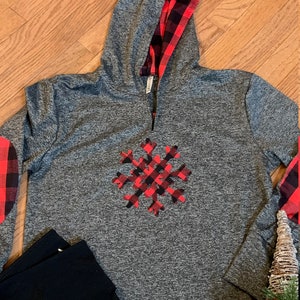 May include: Gray long-sleeve hoodie with a red and black plaid snowflake design on the front. The hoodie has a red and black plaid lining on the hood.