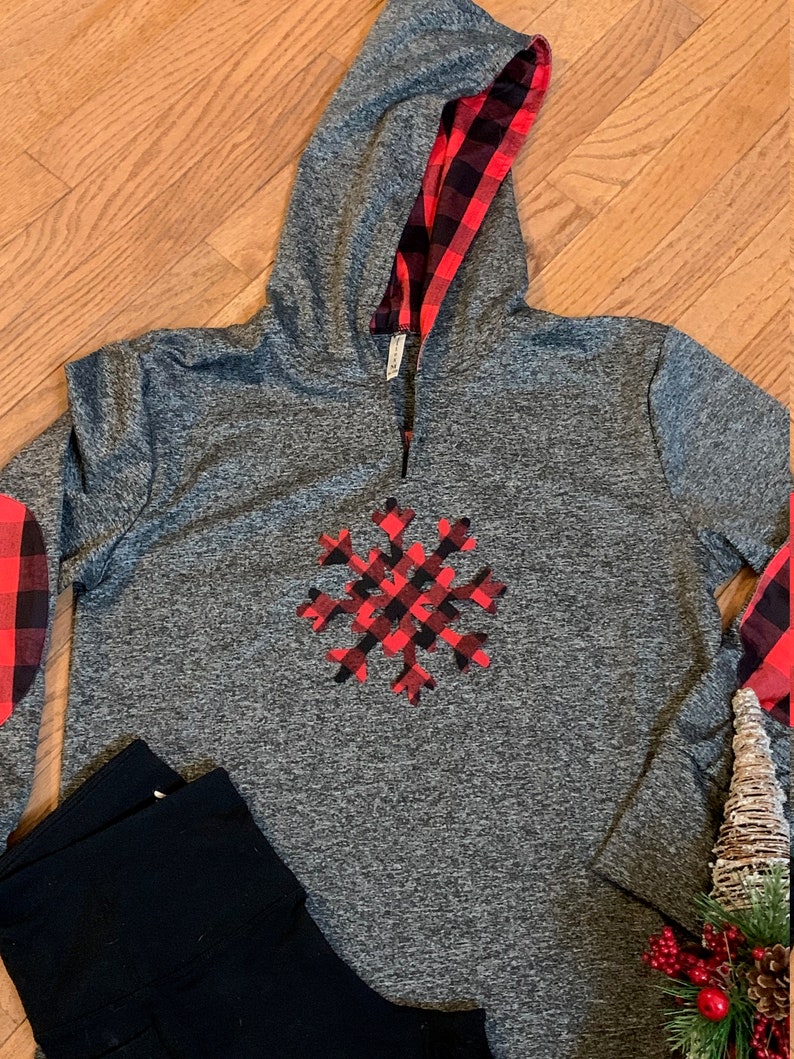May include: Gray long-sleeve hoodie with a red and black plaid snowflake design on the front. The hoodie has a red and black plaid lining on the hood.