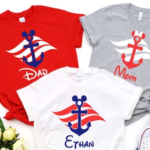 May include: Three white t-shirts featuring a red, white and blue anchor design. The shirts are labelled with the words "Dad", "Mom", and "Ethan".