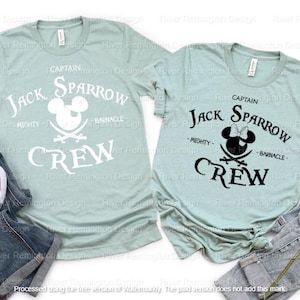 May include: Two light blue t-shirts with a black and white Mickey Mouse pirate design. The text on the shirts reads "Captain Jack Sparrow Crew" with the words "Mighty" and "Barnacle" underneath the pirate Mickey Mouse.