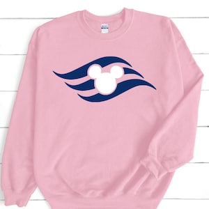 May include: A pale pink sweatshirt with a navy blue and white Mickey Mouse logo. The logo is a stylized design with Mickey Mouse's head in the centre, surrounded by curved lines. The sweatshirt has long sleeves and a crew neck.
