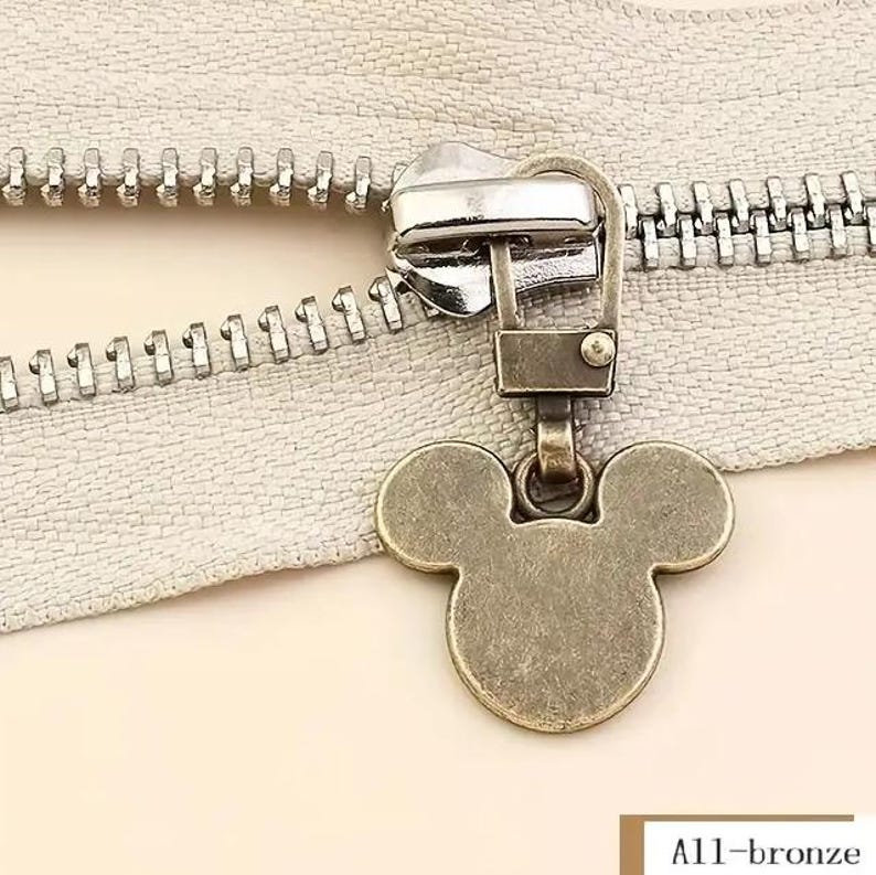 Op de afbeelding: Een bronzen rits-trekker met een Mickey Mouse-ontwerp. De rits-trekker is bevestigd aan een zilveren rits.