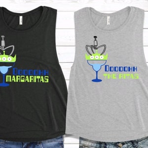 May include: Two sleeveless shirts with a graphic of a margarita glass with a green alien head on top. The text on the black shirt says "Ooooooh Margaritas" and the text on the gray shirt says "Ooooooh The Ritas".