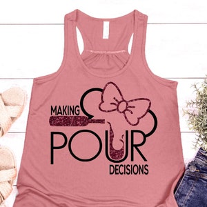 May include: A dusty rose tank top with a black graphic that says "MAKING POUR DECISIONS." The design includes a wine bottle, a wine glass, and a bow. The text and bow have a glittery texture.