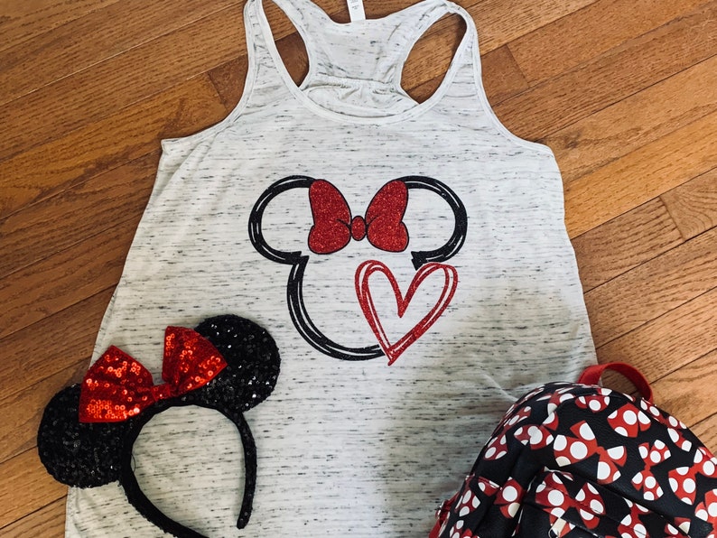 May include: A white tank top with a black and red Minnie Mouse design. The design includes a heart and a bow. A black headband with red sequins and a black and red polka dot backpack are also pictured.