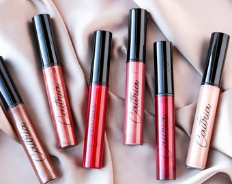 May include: Six tubes of liquid lipstick in various shades of red, pink, and nude. The tubes are all black with white lettering that says "Coutria".