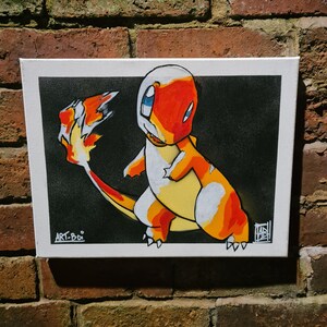 Puede incluir: Un lienzo pintado a mano con una ilustraci&oacute;n de dibujos animados de un Pok&eacute;mon de tipo fuego, Charmander, con un esquema de colores naranja brillante, amarillo y blanco sobre un fondo negro. La obra de arte est&aacute; firmada "ART-BOI" en la esquina inferior izquierda.