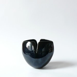 Puede incluir: Un jarrón de cerámica azul oscuro con un diseño único de abertura superior. El jarrón tiene forma de capullo de flor, con un acabado liso y brillante.