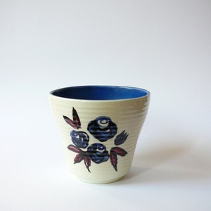May include: A white ceramic planter with a blue rim and a floral design featuring blue and red flowers.