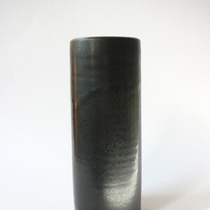 May include: A black ceramic vase with a smooth, glossy finish. The vase is cylindrical in shape and has a slightly rounded bottom.