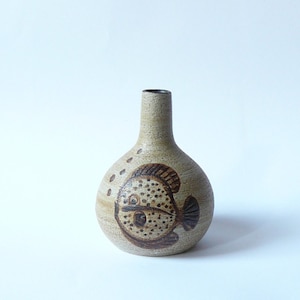 May include: A small, light brown ceramic vase with a brown fish design. The vase has a round body and a narrow neck.