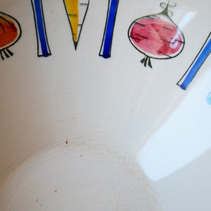 May include: White ceramic bowl with a blue and black rim. The bowl is decorated with hand-painted vegetables, including a carrot, a red onion, and a green pepper.