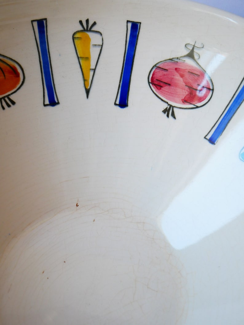 May include: White ceramic bowl with a blue and black rim. The bowl is decorated with hand-painted vegetables, including a carrot, a red onion, and a green pepper.