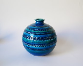 May include: A blue and green ceramic vase with a round body and a textured surface. The vase has a wide mouth and a narrow neck.