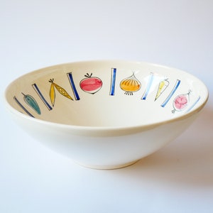May include: A white ceramic bowl with a blue and yellow vegetable design. The bowl has a wide rim and a rounded bottom.
