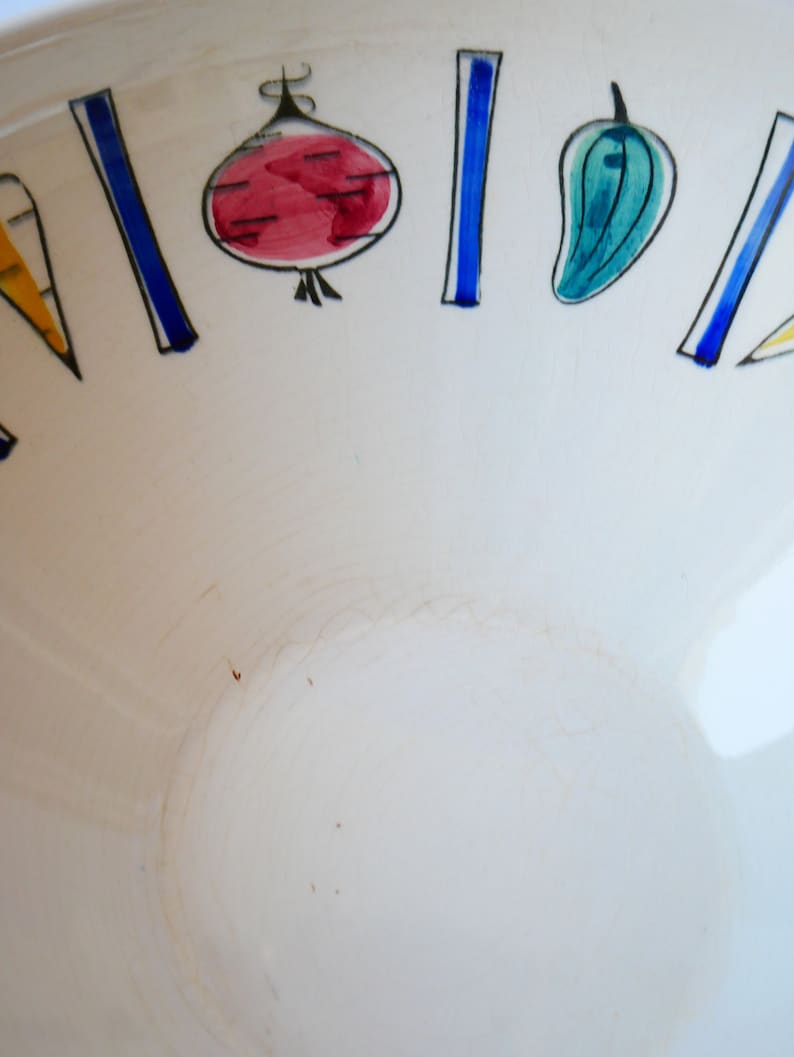 May include: White ceramic bowl with a blue and white rim. The rim is decorated with a repeating pattern of stylized vegetables in red, yellow, green, and blue.