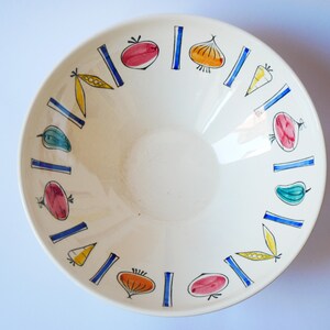 May include: A white ceramic bowl with a blue and yellow rim. The bowl is decorated with a pattern of vegetables, including tomatoes, onions, peppers, and peas.