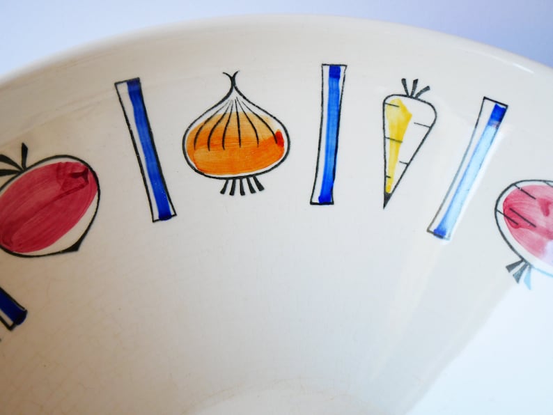 May include: White ceramic bowl with a colorful vegetable design. The bowl features red, orange, yellow, blue, and black painted vegetables, including a carrot, onion, and beets.