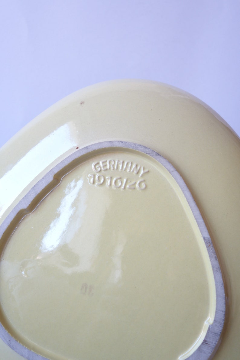 Op de afbeelding: Een gele keramische serveerschaal met een driehoekige stempel op de bodem met de tekst "GERMANY 1916126".
