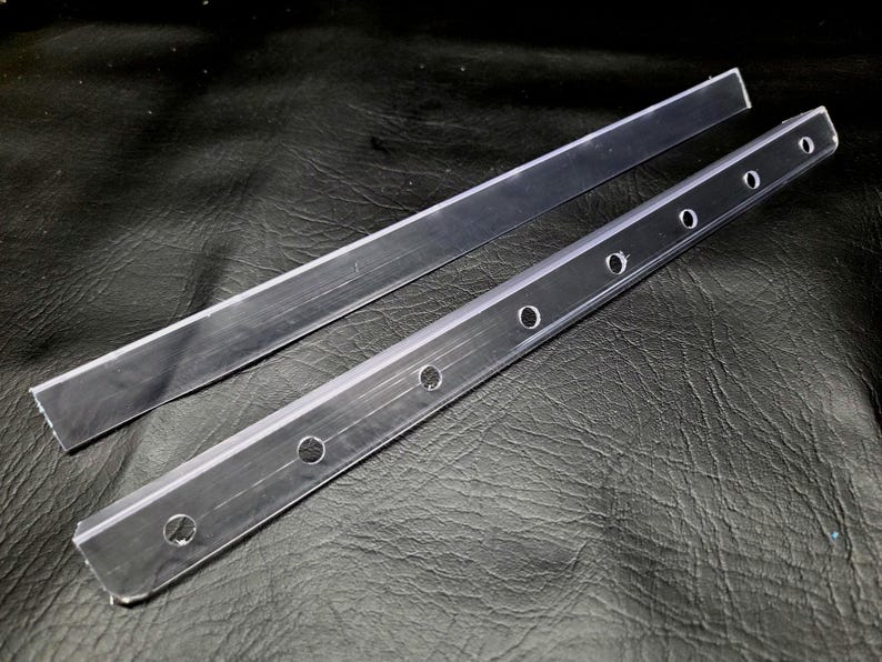 K&ouml;nnte beinhalten: Zwei klare, starre Acrylstreifen. Ein Streifen ist glatt mit einer geraden Kante. Der zweite Streifen weist eine Reihe von gleichm&auml;&szlig;ig verteilten, kreisf&ouml;rmigen L&ouml;chern auf, die entlang der L&auml;nge zur Befestigung eingestanzt sind.