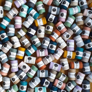 May include: A collection of colorful spools of string, each with the word "Bobbiny" printed on the label. The spools are arranged in a random pattern on a wooden surface.
