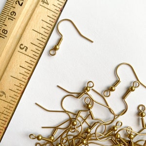 May include: A pile of gold-toned earring hooks with a ruler in the background. The ruler is marked in inches.