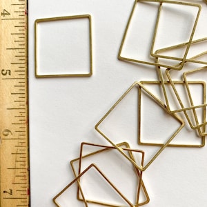 May include: A group of gold-coloured metal square frames of various sizes. The frames are arranged in a random pattern on a white surface.