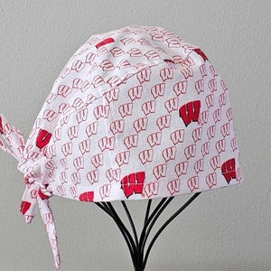 May include: White surgical scrub hat with a red and white pattern of the letter "W".