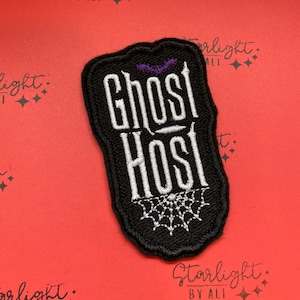 May include: Black embroidered patch with white text that reads "Ghost Host" and a purple bat and spider web design.