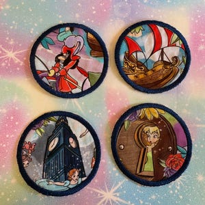 以下が含まれることがあります： 青いステッチの縁取りが付いた、4つの丸い布製パッチ。各パッチには、子供向けの物語の異なる画像が描かれています。フック船長、海賊船、ビッグベン、ピーターパン。背景はカラフルな模様の生地です。