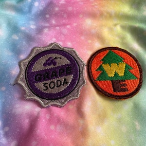 May include: Two embroidered patches. One is a purple and silver grape soda patch with a grape image. The other is a brown, orange, and green patch with a tree and the letter W.