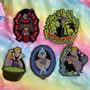 May include: Five embroidered iron-on patches featuring Disney villains. The patches are on a rainbow-colored fabric background. The villains are Ursula, Hades, Maleficent, Evil Queen, and Captain Hook.