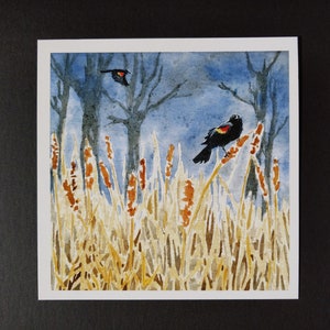Peut inclure: Peinture &agrave; l'aquarelle de deux oiseaux noirs avec des marques rouges perch&eacute;s sur de hautes roseaux bruns. Les oiseaux sont sur un fond de ciel bleu avec des arbres en arri&egrave;re-plan.
