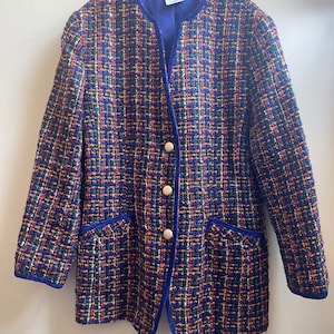 May include: A blue tweed jacket with a colorful plaid pattern. The jacket has a velvet trim and gold buttons. The label reads "KLASON".