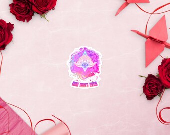 May include: A sticker with a colorful design featuring a lotus flower with an eye in the center, surrounded by vibrant pink, purple, and blue hues. The text "GOD MAN'S EYES" is below the design. The sticker is on a pink surface with red roses and origami.