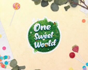 May include: A green, grassy circle with the text "One Sweet World" in blue and white lettering. The circle is surrounded by white daisies and butterflies.
