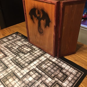 May include: A wooden game board with a black dragon design on the front. The board is closed and has a black and white dungeon map on the table.