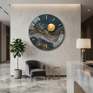 May include: A large circular wall clock featuring a dark blue and gold abstract landscape design. The clock face displays a golden sun, a stylized tree, and gold hour markers. Thin gold hands indicate the time against a glossy, reflective surface.