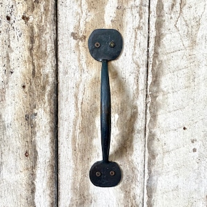 May include: Black metal door handle with a rounded top and bottom. The handle is attached to a white wooden door.