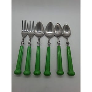 May include: A set of six vintage stainless steel flatware pieces: two forks and four spoons. Each piece has a bright green handle. The utensils are arranged on a white surface.