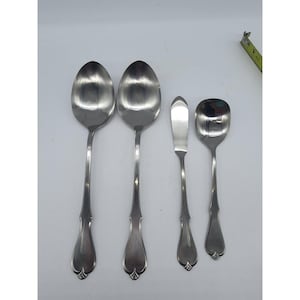 May include: A set of four stainless steel utensils including two large oval spoons, one butter knife with a flat blade, and one small square-ended spoon. A yellow measuring tape is visible in the corner, showing a length of approximately 1 inch.