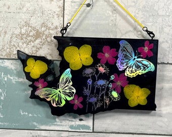 May include: A black resin outline of the state of Washington with iridescent butterflies and pressed flowers in yellow and pink.