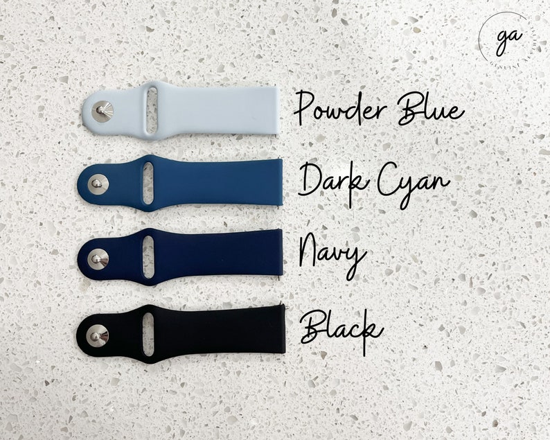 Pu&ograve; includere: Quattro cinturini per orologi in azzurro polvere, ciano scuro, blu navy e nero. Ogni cinturino ha un perno color argento e i nomi dei colori sono scritti in corsivo. I cinturini sono disposti su una superficie bianca maculata.
