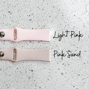 Pu&ograve; includere: Due cinturini per orologi in silicone rosa chiaro e rosa sabbia. Il cinturino rosa chiaro &egrave; in alto e quello rosa sabbia sotto. Il testo "Light Pink" e "Pink Sand" &egrave; scritto in corsivo accanto a ciascun cinturino.