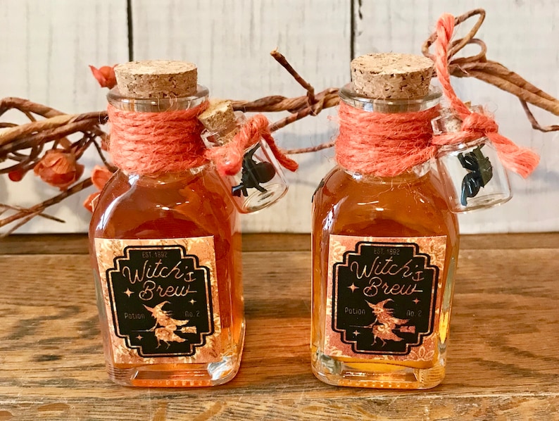 Pu&ograve; includere: Due piccole bottiglie di vetro con tappi di sughero e spago arancione legato attorno al collo. Le bottiglie sono riempite con un liquido dorato e hanno etichette nere che recitano "Witch's Brew Potion No. 7".